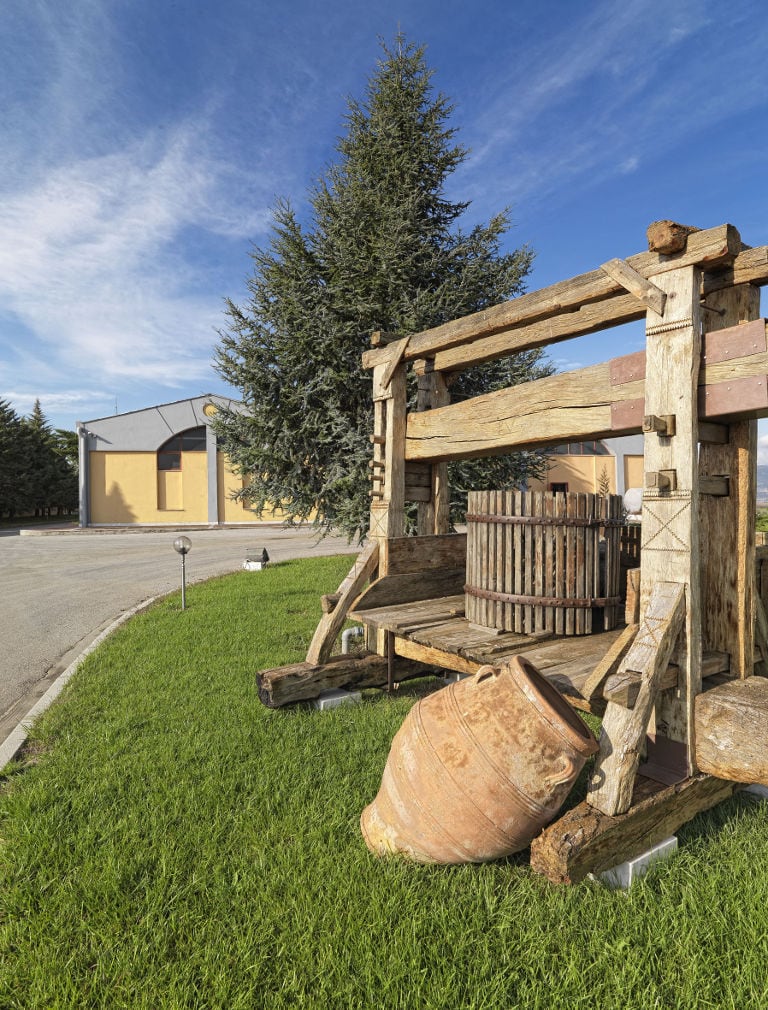 manual old grape press on the green lawn and a amcient amphora outside at Domaine Costa Lazaridi Drama